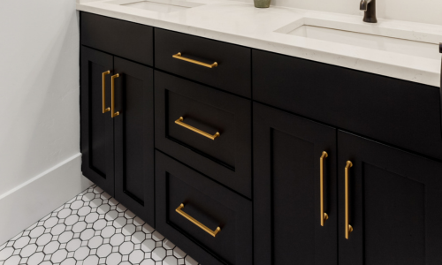A close-up of black bathroom cabinets with gold hardware.