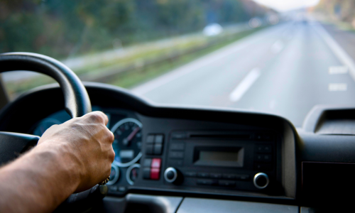 A close up of hands on the steering wheel of a vehicle driving down the road.