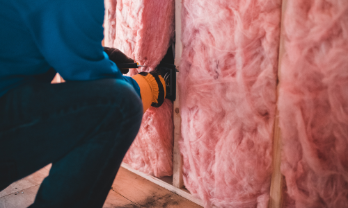 Pink insulation being rolled out into. a wall.