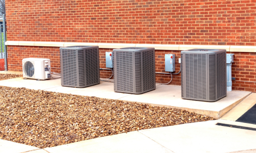 Three HVAC units on the side of a brick building on a clear day.