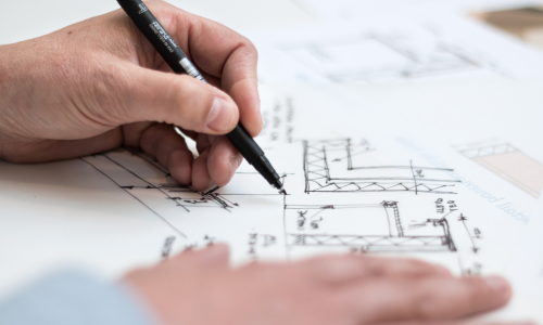 A close up of hands holding a pen writing on a blueprint.