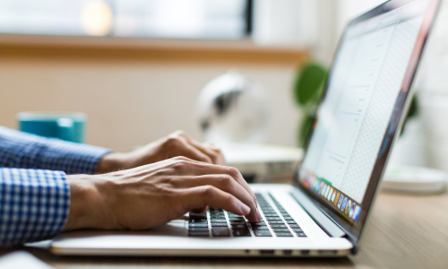 A close up of hands typing on a laptop.